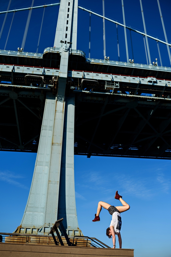 A woman doing a perfect handstand in philadelphia under the Ben Franklin Bridge.